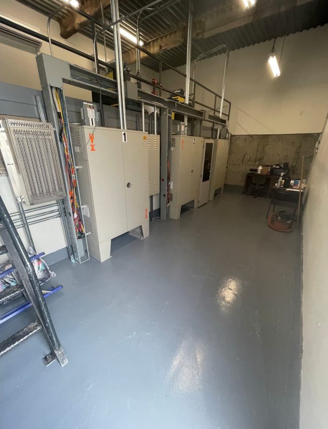 Elevator control cabinets and conduit above a clear gray machine-room floor.