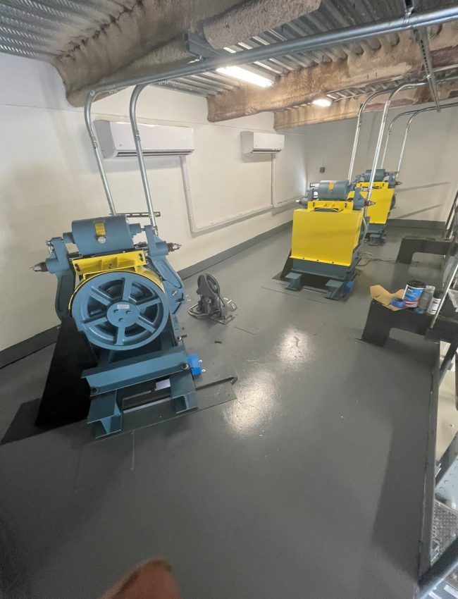 Elevator machinery with blue sheaves and yellow guards in a finished machine room.